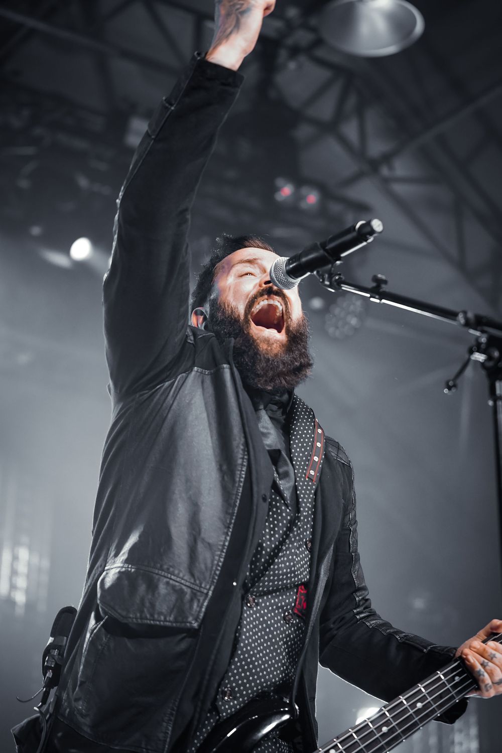 A performer in a black leather jacket sings passionately on stage during a concert with dramatic lighting.