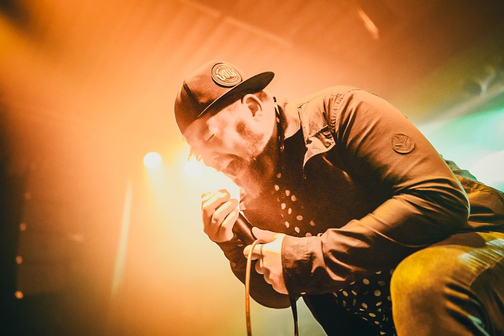 A musician performs on stage with dramatic orange and teal lighting creating an atmospheric concert environment.
