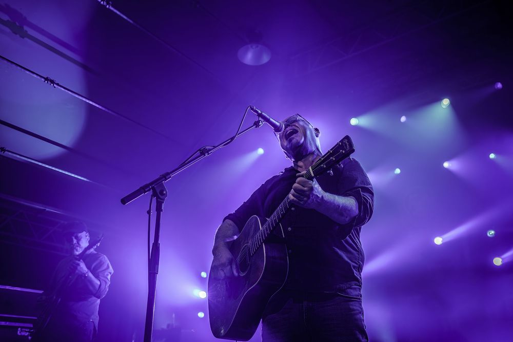 A performer sings passionately on stage bathed in dramatic purple lighting during a concert performance.