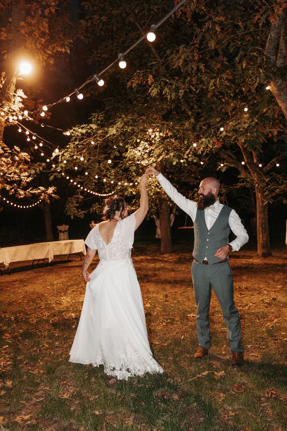 Bride and groom dance under string lights in garden at romantic nighttime wedding reception.