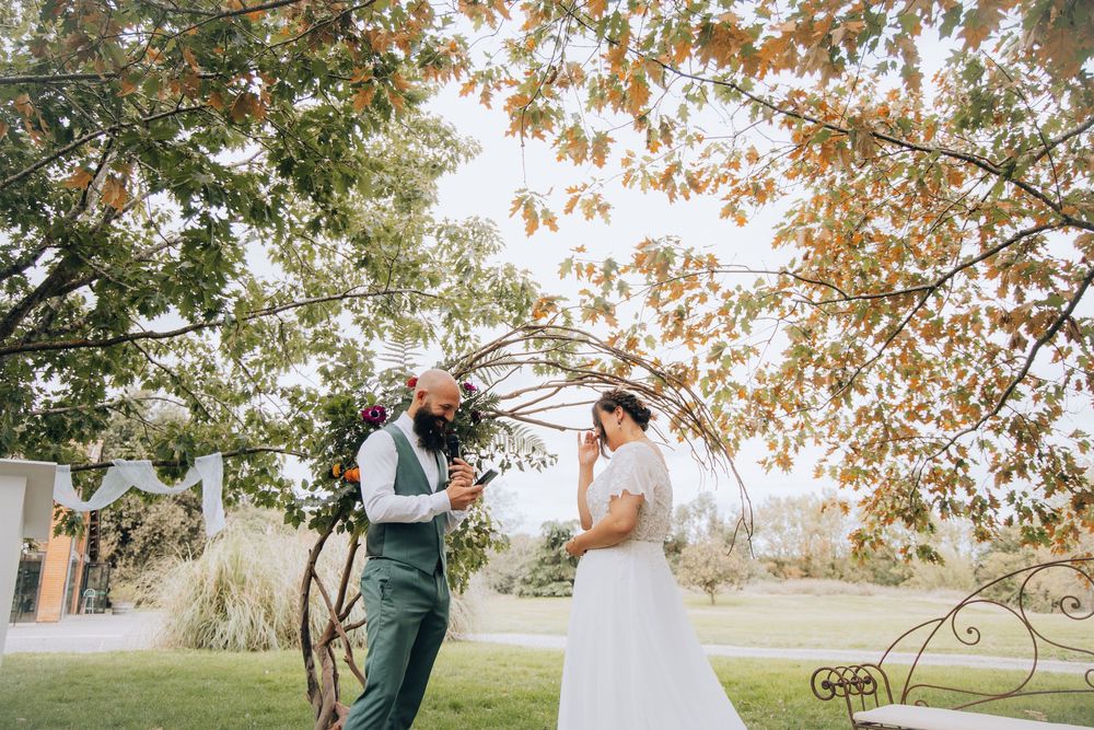 Bride and groom laugh joyfully together beneath a canopy of autumn leaves during their outdoor wedding.