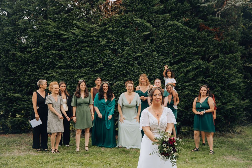Bride prepares to toss her bouquet to a large group of female wedding guests on a lush green lawn.