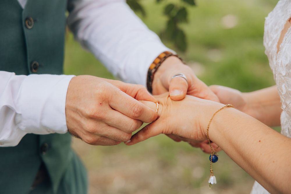 Groom places a gold wedding band on the bride's finger during an intimate outdoor ring exchange ceremony.