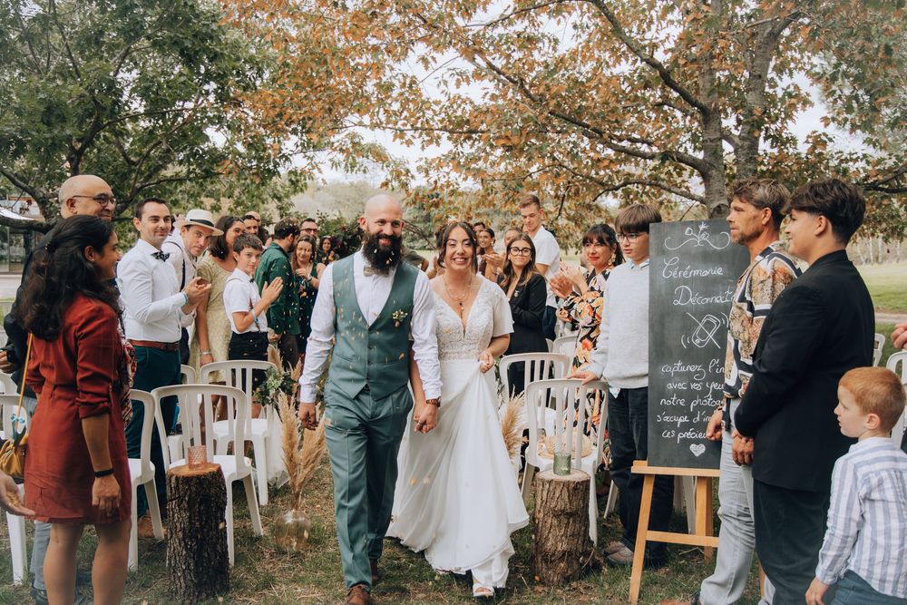 Happy newlyweds walk down aisle surrounded by cheering guests at outdoor fall wedding.