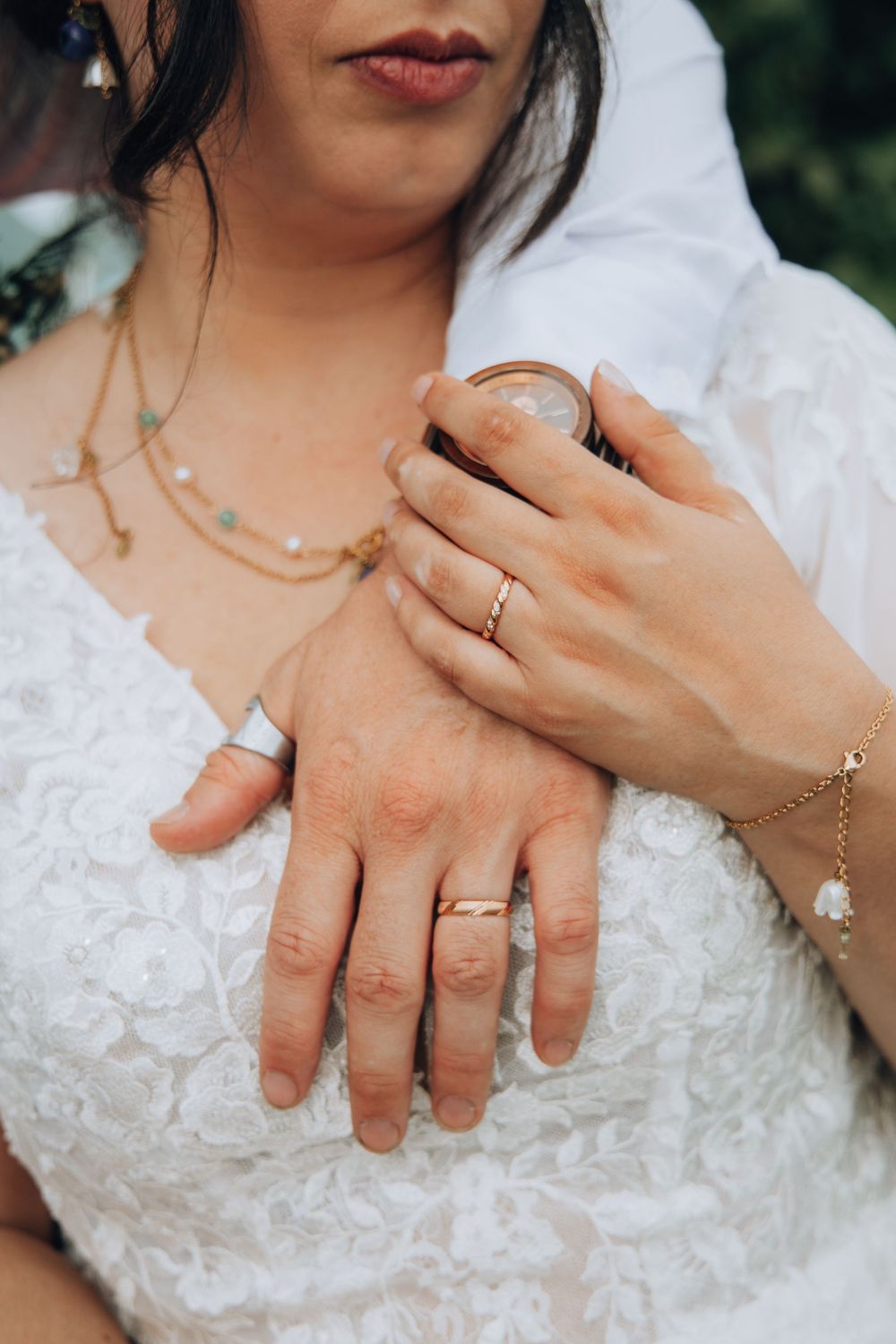 Close-up of bride and groom hands showing wedding rings and gold jewelry.
