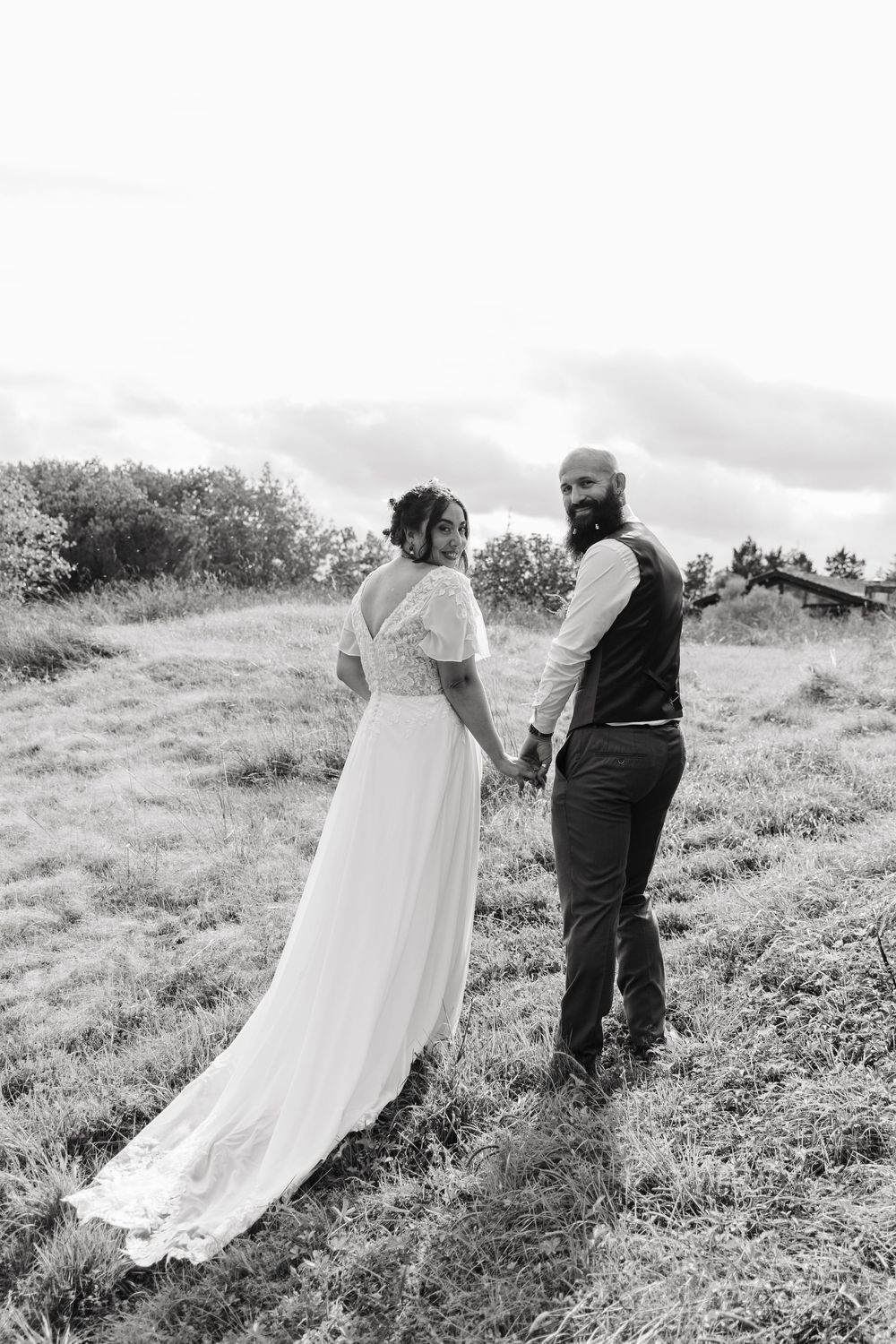 Black and white photo of bride and groom holding hands walking through open countryside.