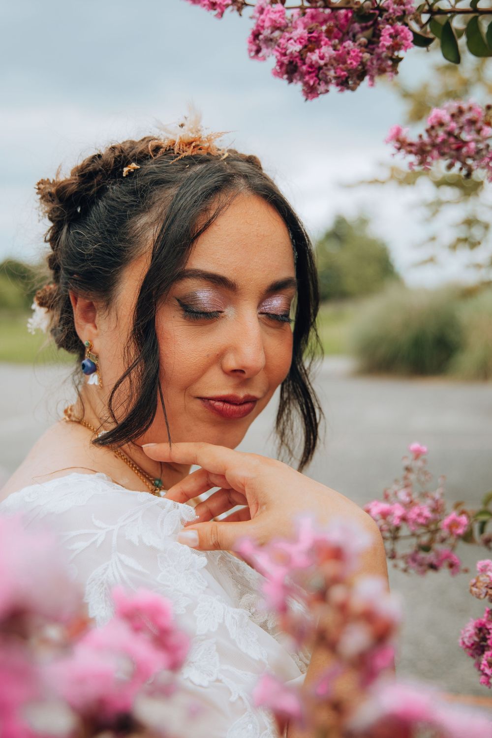 Beautiful bride with elegant updo and blue earrings poses gracefully among pink flowering branches.