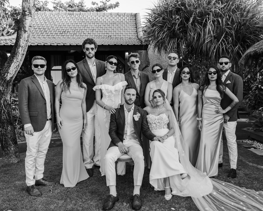 A wedding party poses together in matching gray attire at an outdoor venue.