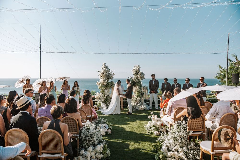 Panoramic view of outdoor wedding ceremony with guests seated facing ocean vista.