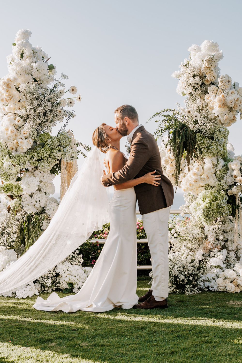 Wedding couple dancing on green lawn with white floral arrangements and draping in the background.