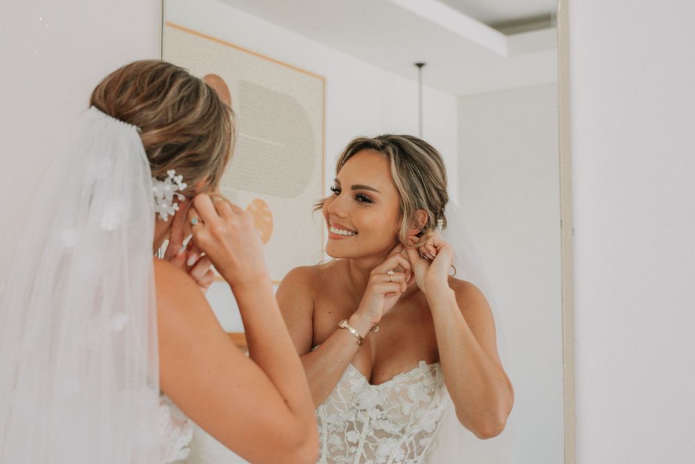 A bride in an elegant lace wedding dress adjusts her earrings while getting ready for her special day.