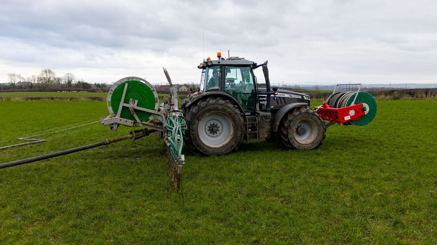 Tractor spraying agricultural fertilizer or pesticides on green farmland with long boom sprayer attachment.