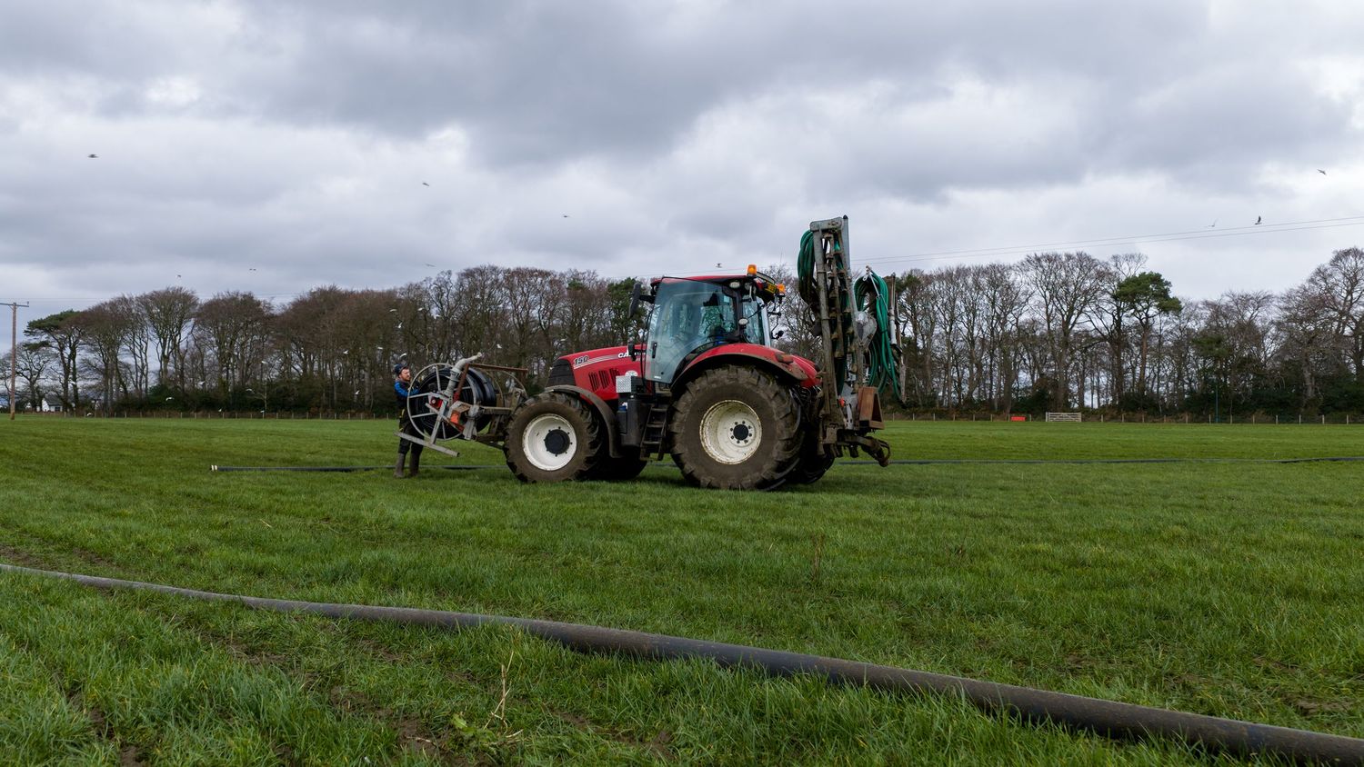 Panoramic view of farm tractors working in green agricultural fields with trees along the horizon.