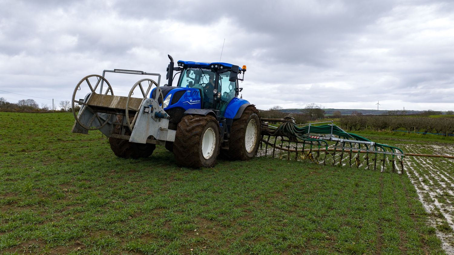 Tractor towing agricultural equipment across a green field under cloudy skies.