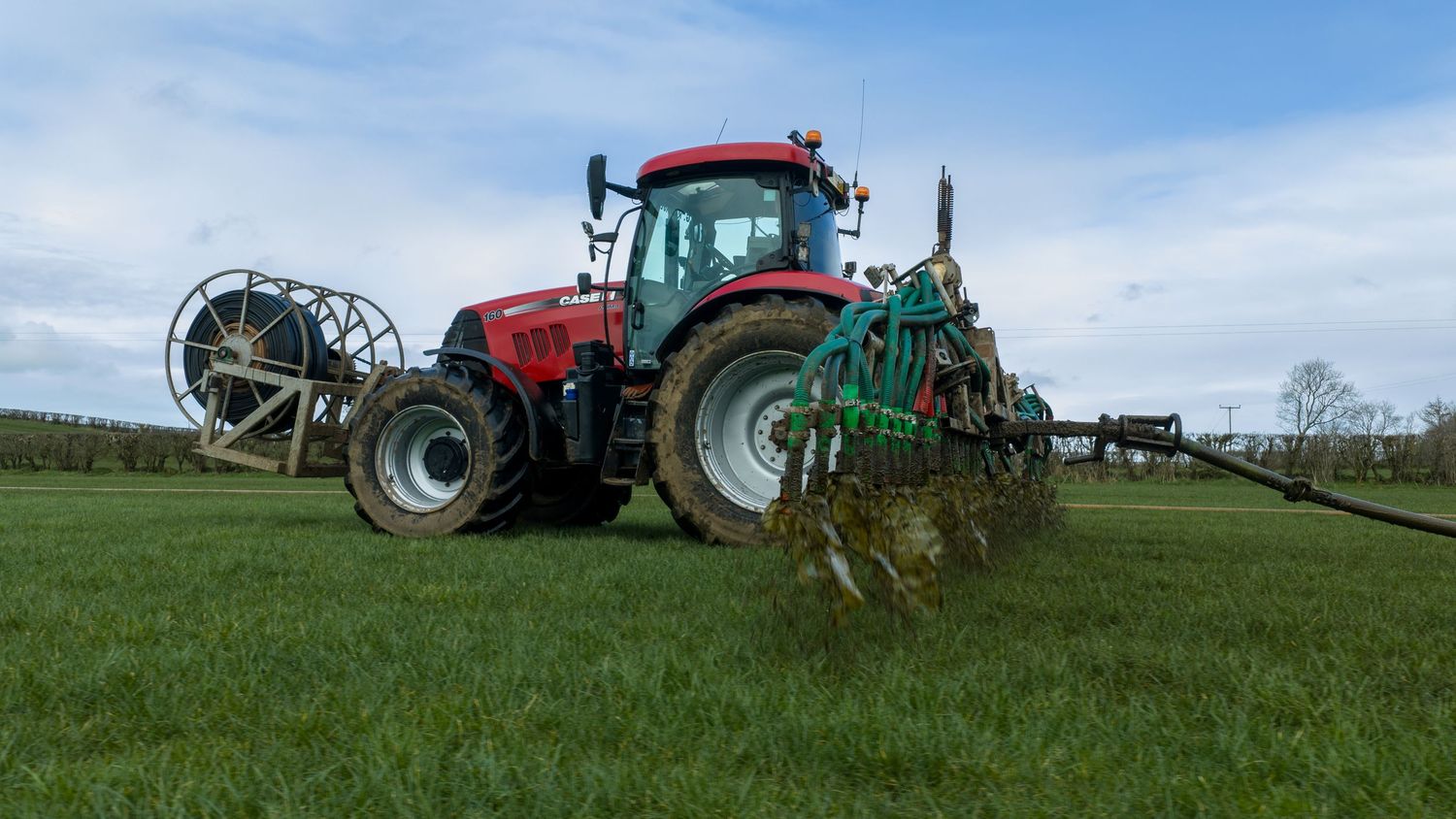 A panoramic view of red and green tractors working in agricultural fields under a bright blue sky.