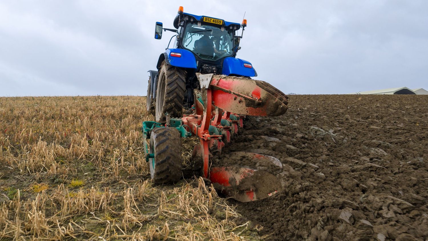 Agricultural tractors plowing dark soil in a field during cloudy weather conditions.