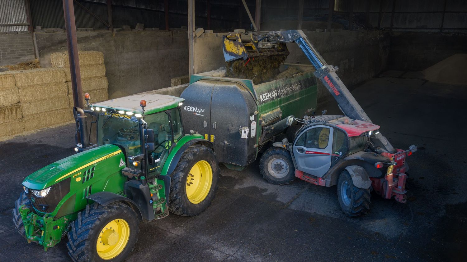 A line of farming tractors and agricultural equipment parked in a dark warehouse or storage facility.