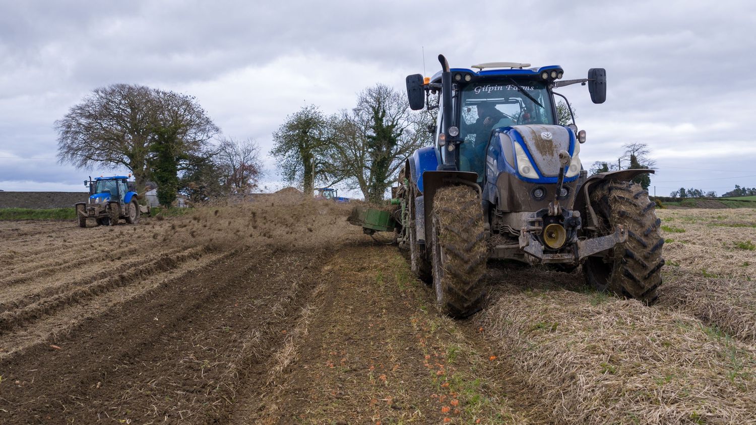 A panoramic view of agricultural machinery plowing and preparing farmland under an overcast sky.