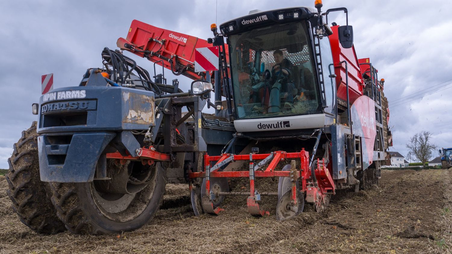 A panoramic view of agricultural machinery and equipment lined up on dirt terrain against a cloudy sky.