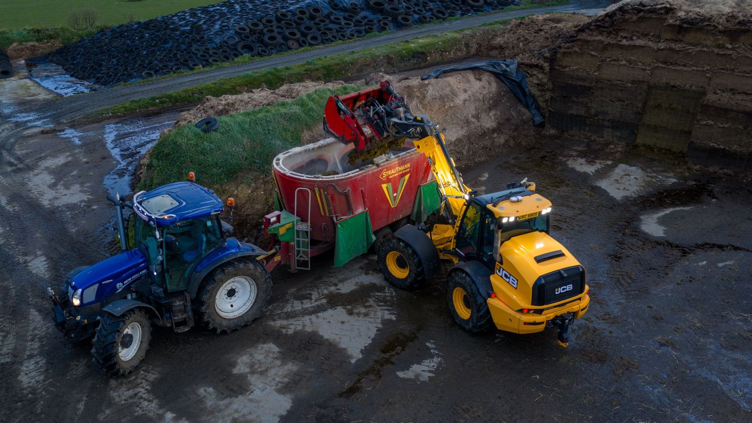 Aerial view of a blue New Holland tractor and yellow wheel loader working together at a construction site.