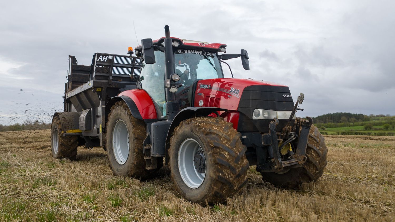 Red Case IH tractor with dump trailer working in a harvested field under overcast skies.