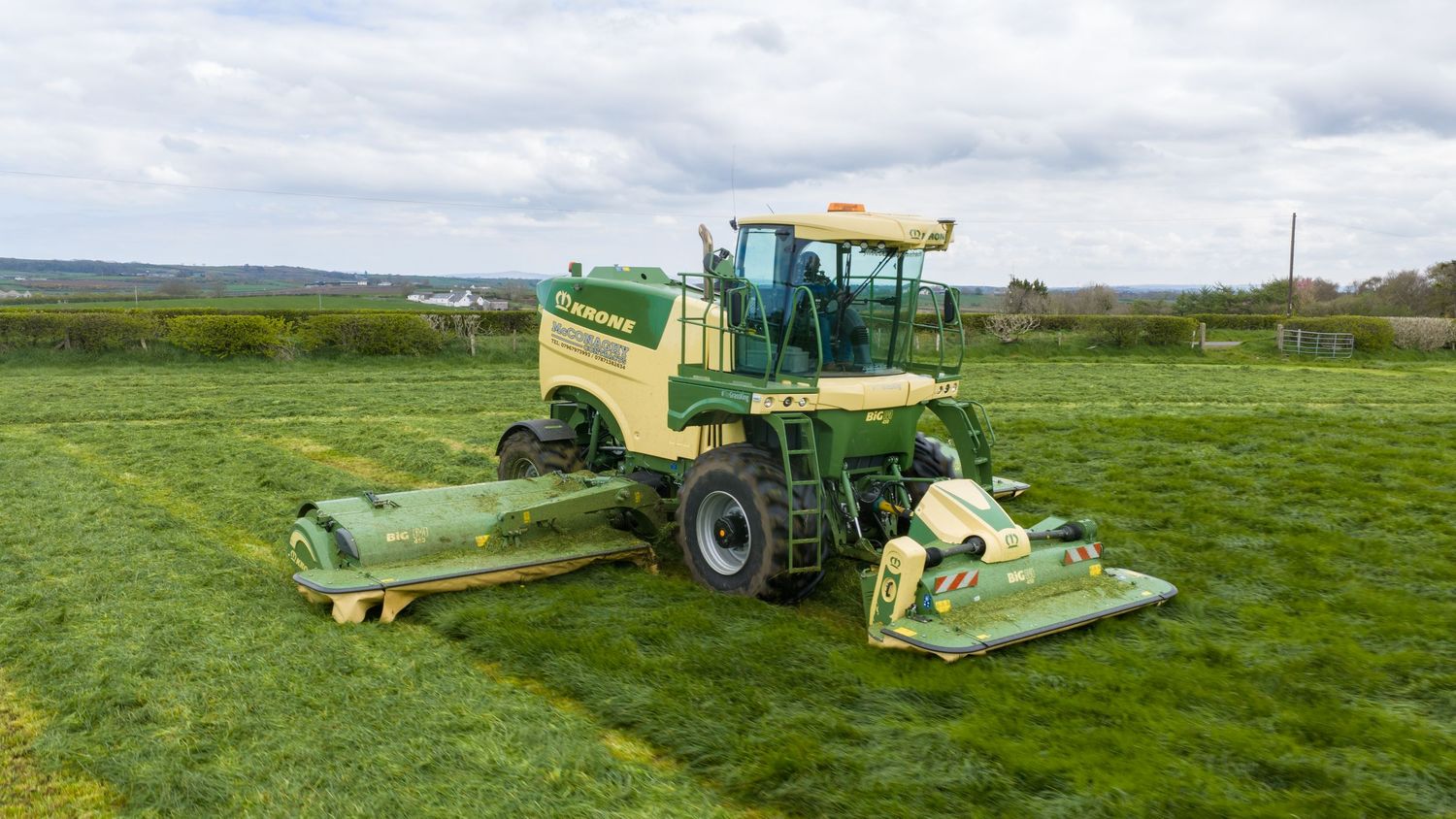 Green Krone self-propelled mower harvesting lush grass in an open field on a clear day.