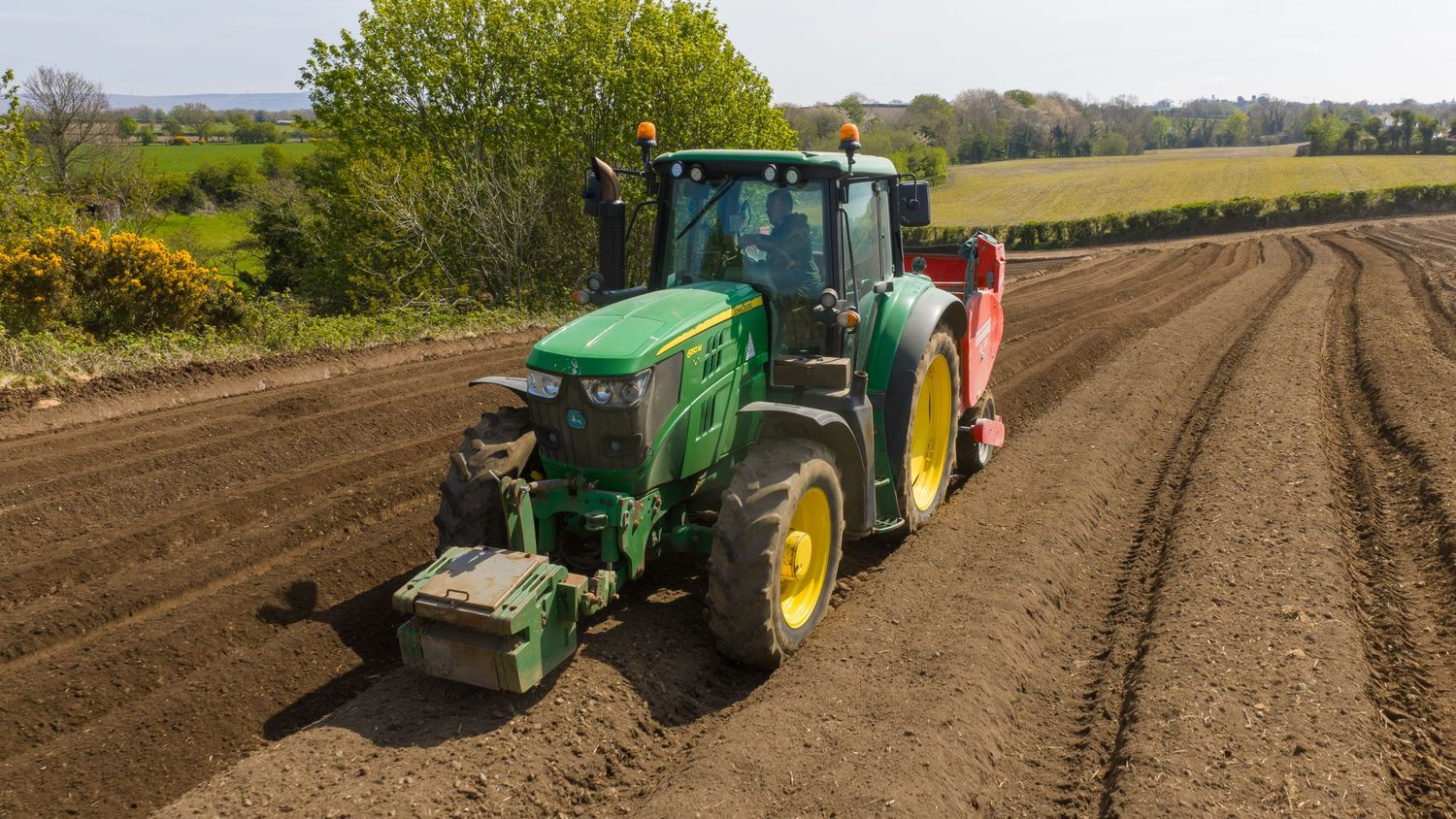 Green John Deere tractor plowing agricultural field, creating neat furrows in rich brown soil on a sunny day.
