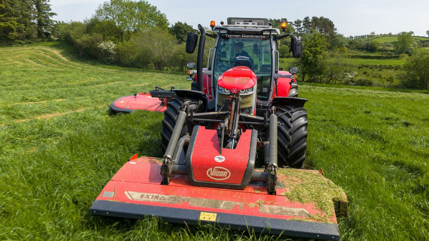 Red Massey Ferguson tractor with front and rear mowers cutting green grass in a rural field.