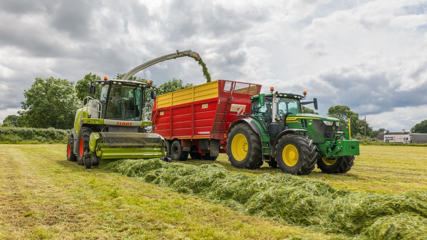 Green CLAAS forage harvester and John Deere tractor collecting freshly cut grass silage in a field.