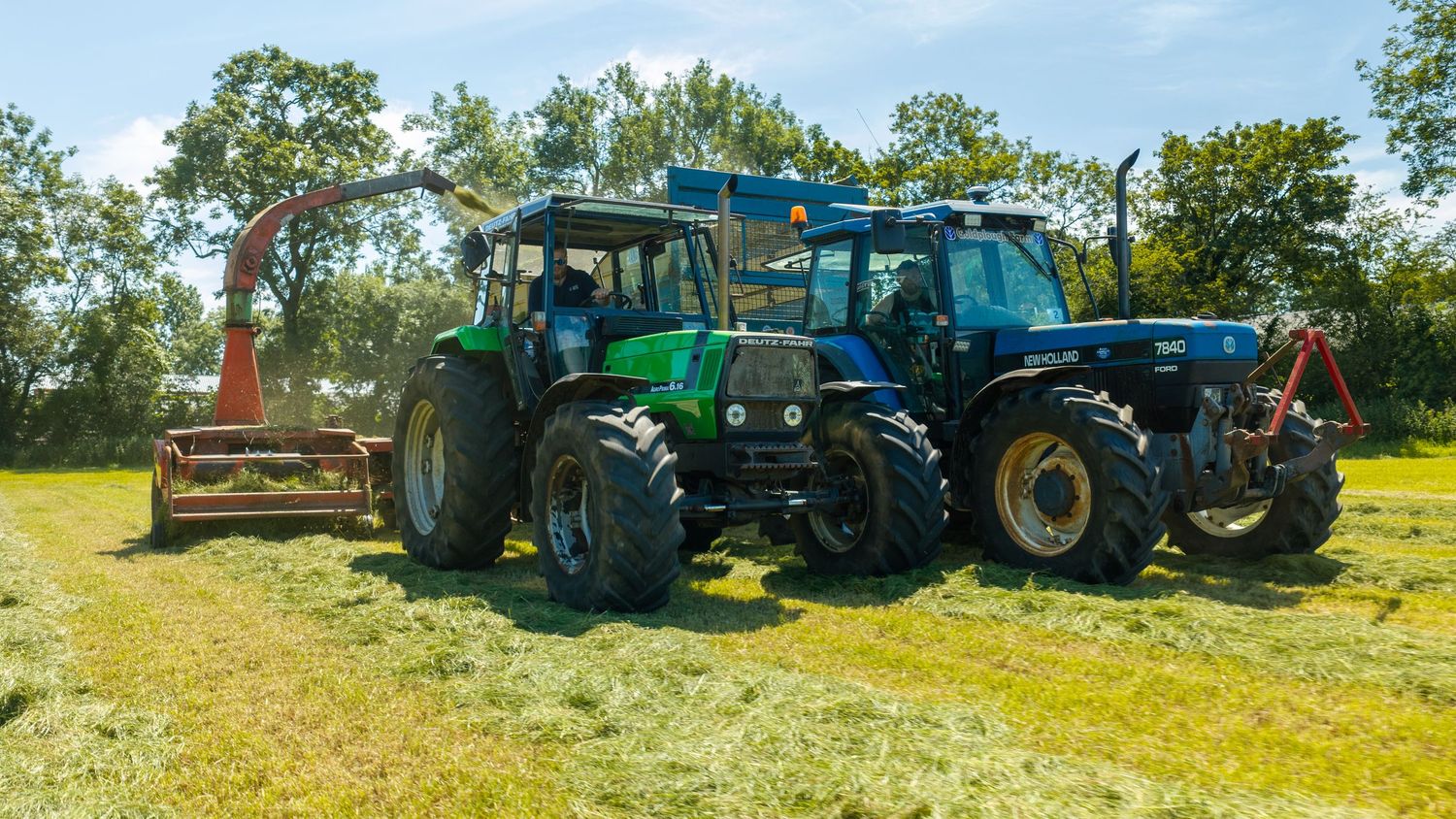 Two tractors parked on a green field surrounded by trees on a sunny day.