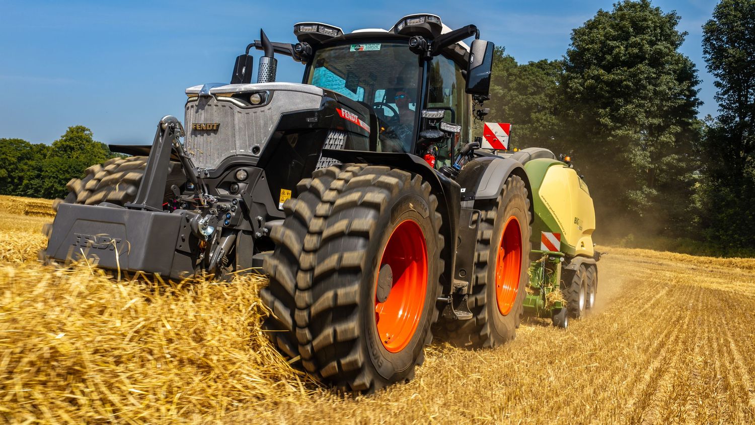 A modern black Fendt tractor with red wheels harvesting in a golden wheat field on a sunny day.