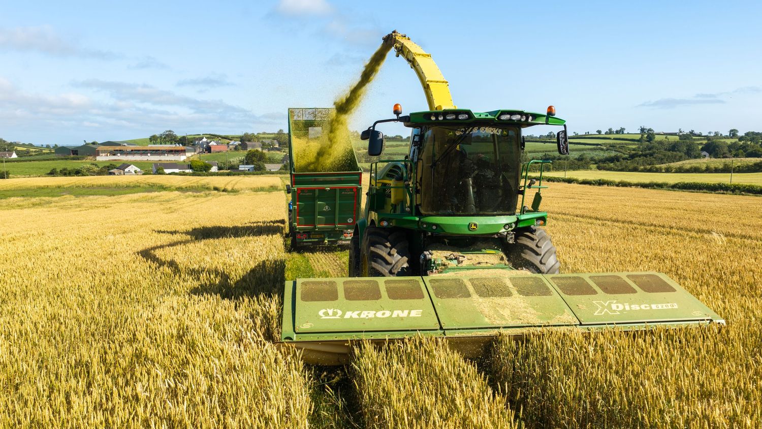 John Deere harvester cutting golden wheat field on a sunny day in rural Ireland.