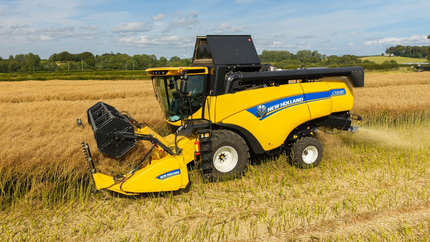 New Holland yellow combine harvester cutting wheat in a green field on a sunny day.