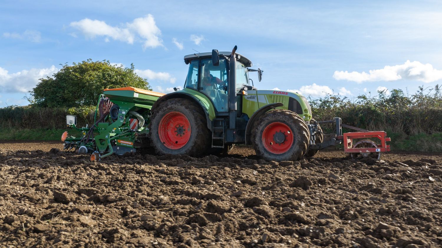 A green Fendt tractor plowing and seeding a large agricultural field on a sunny day.