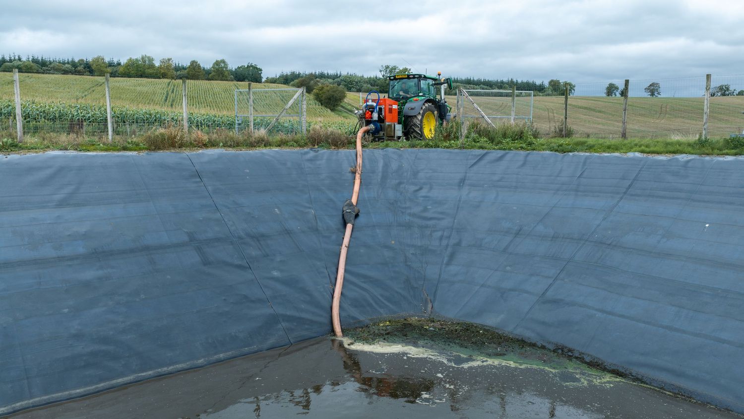A tractor pumping water into a lined agricultural reservoir on a farm field.