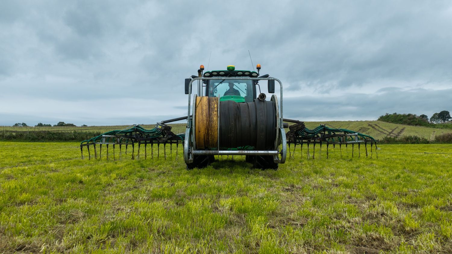 A large agricultural sprayer machine working across a lush green field under an overcast sky.