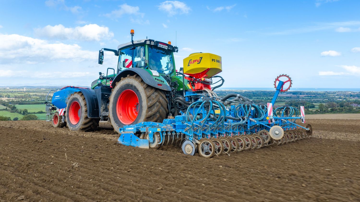 A blue Fendt tractor with red wheels pulling a Lemken precision seeder across a freshly tilled agricultural field.