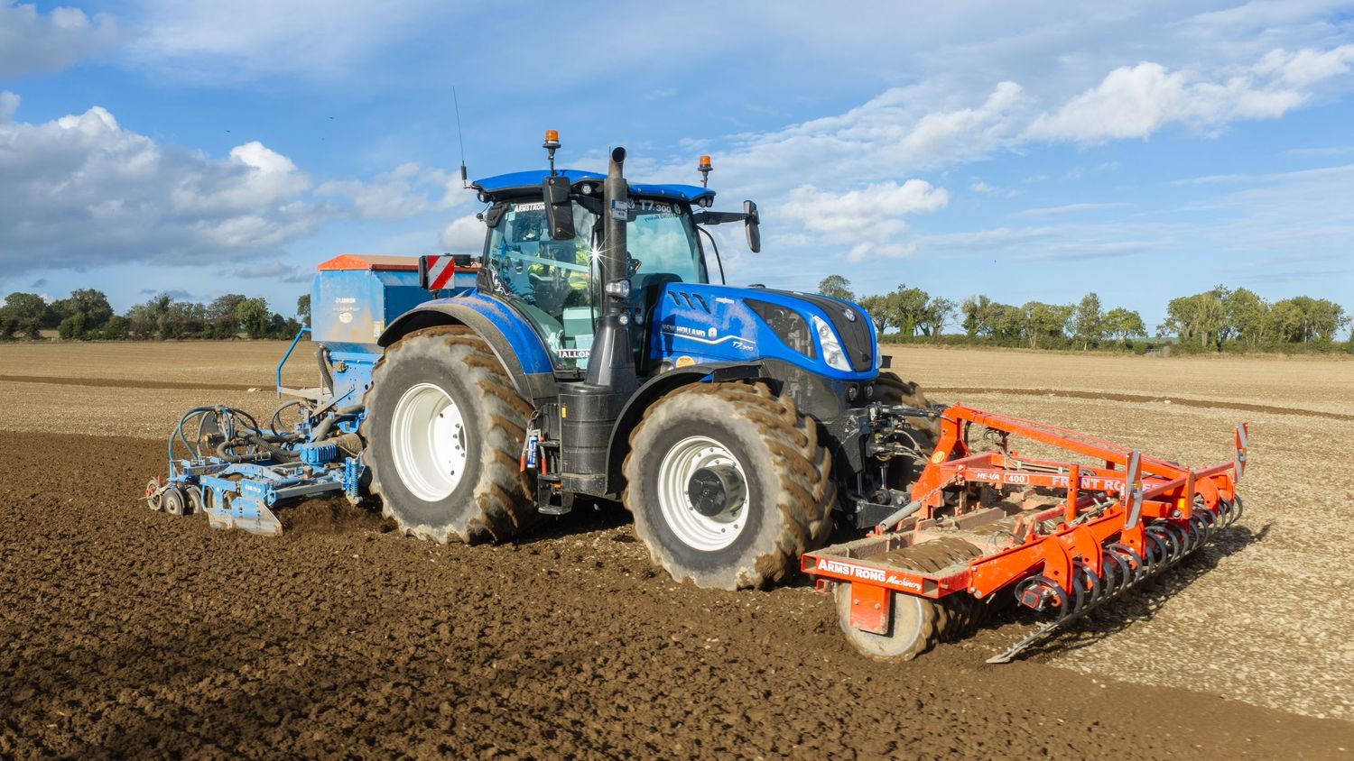 Blue New Holland tractor with agricultural equipment plowing a field on a sunny day.