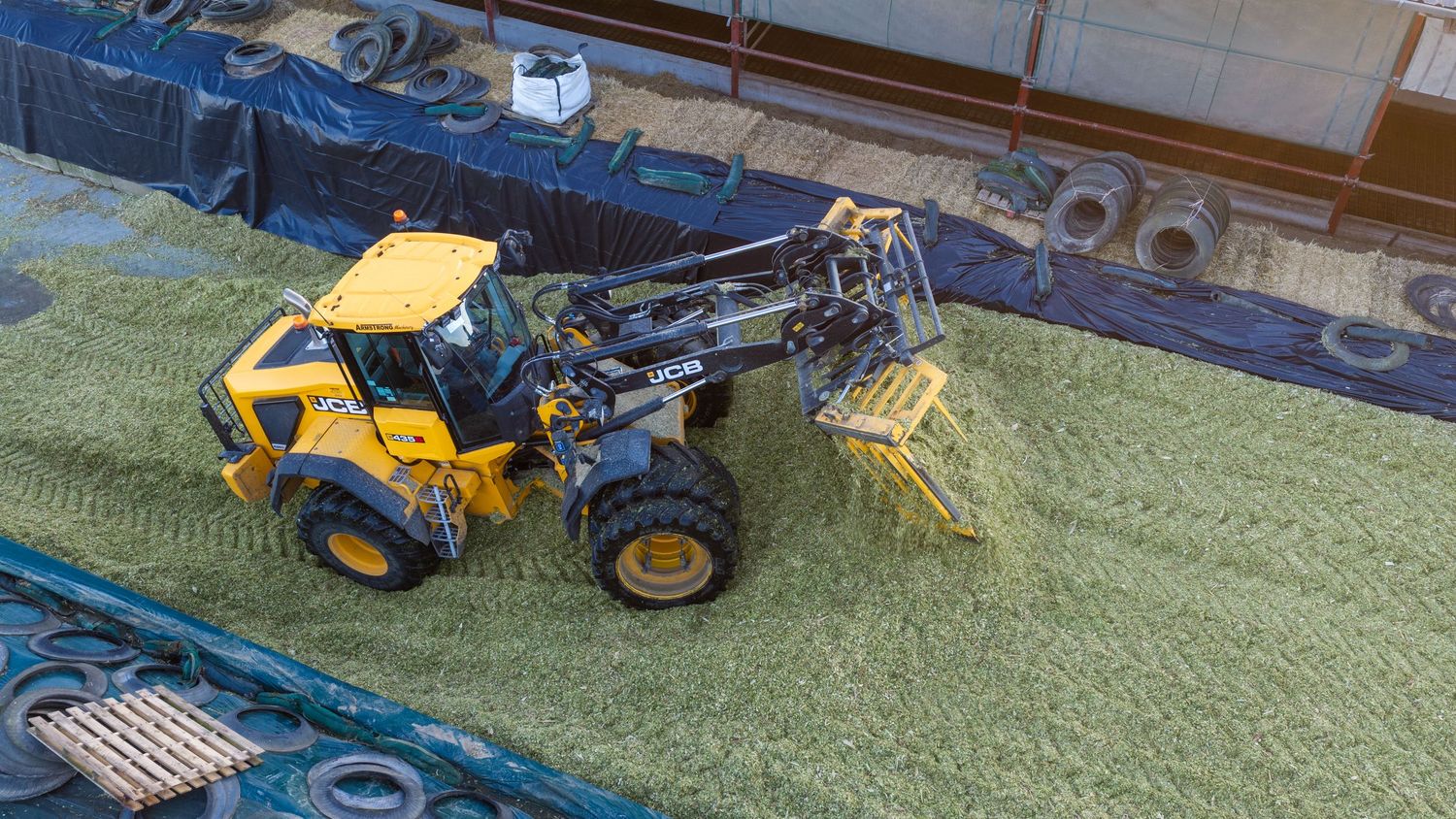Yellow wheel loader installing artificial turf on a sports field, viewed from above.