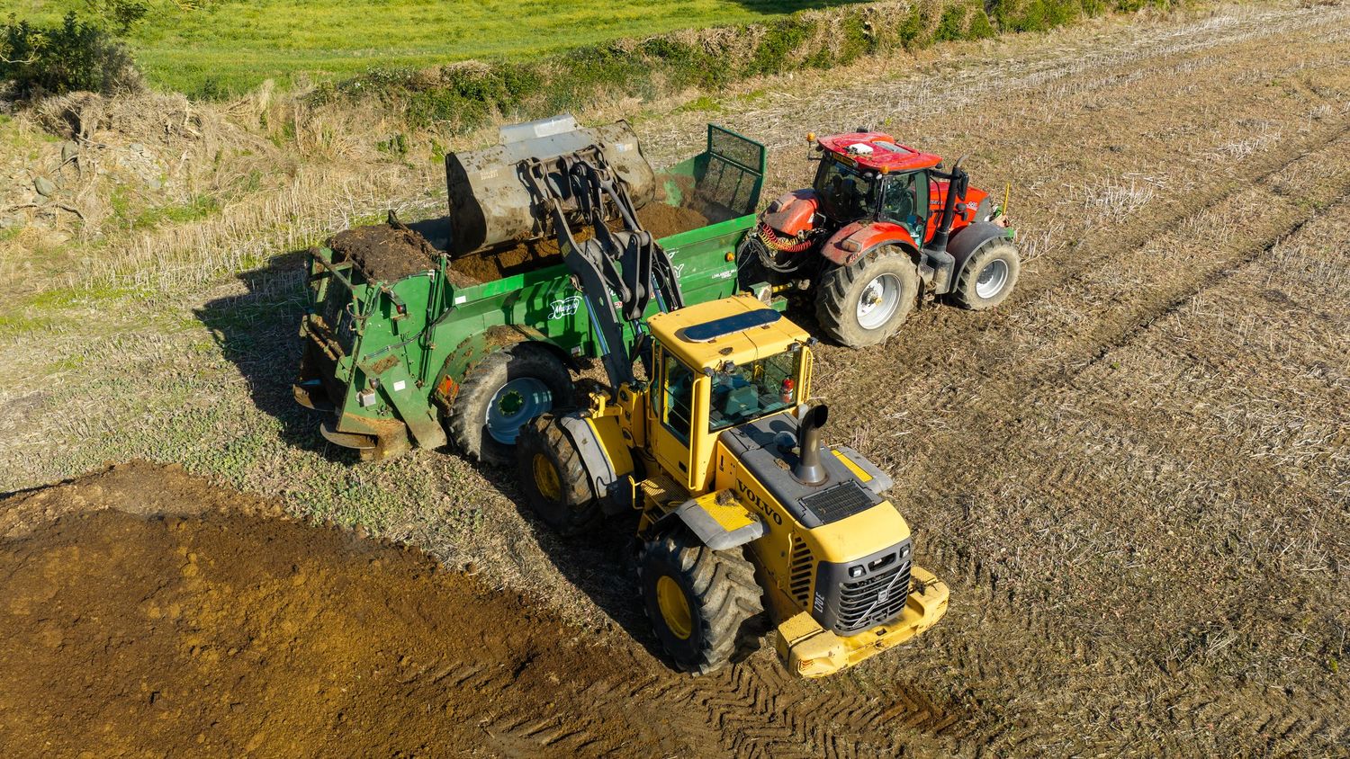 Aerial view of green John Deere and red tractors working together in a muddy agricultural field.