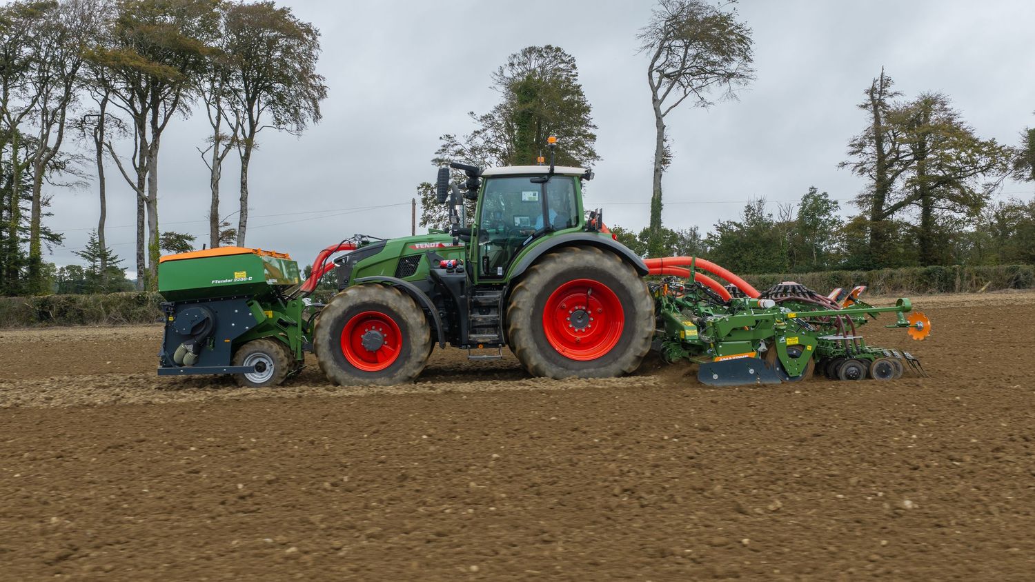 Green Fendt tractor with red wheels pulling agricultural seeding equipment across a plowed field.