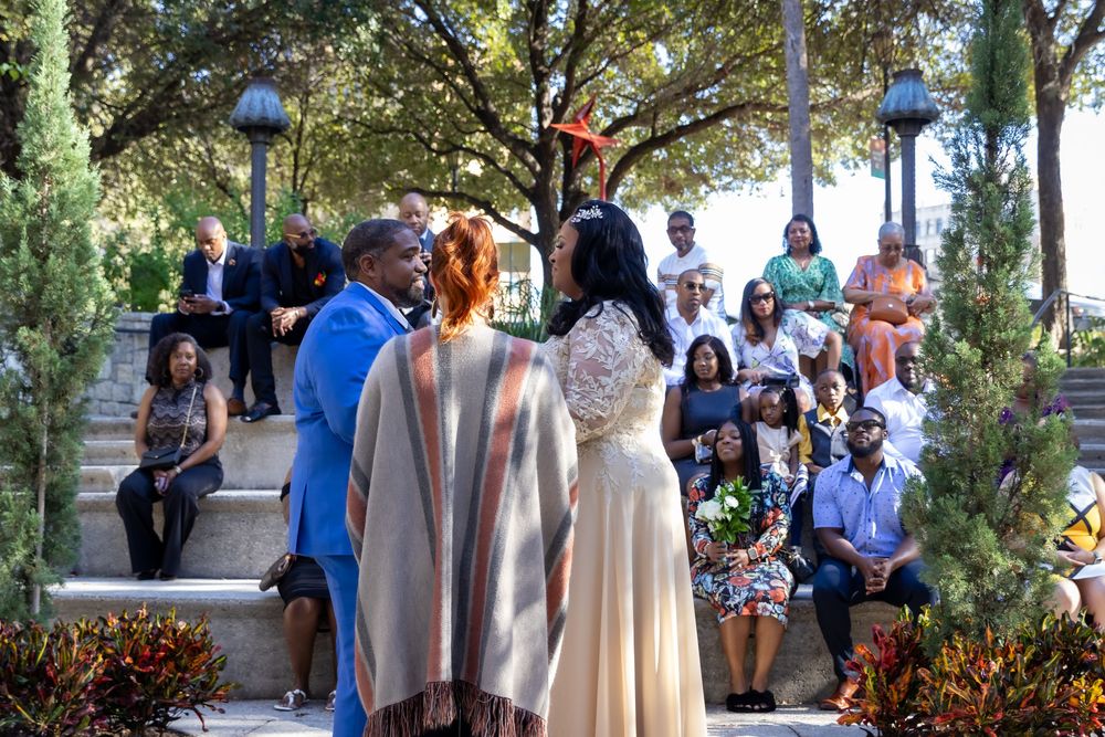 Wedding party gathers outdoors in a garden setting with bridesmaids in soft neutral dresses and groomsmen in suits.