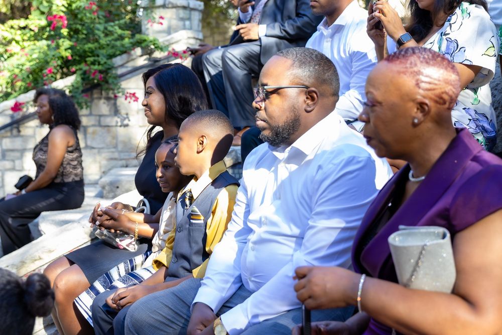 A group of spectators watch intently from the sidelines during an outdoor event on a sunny day.