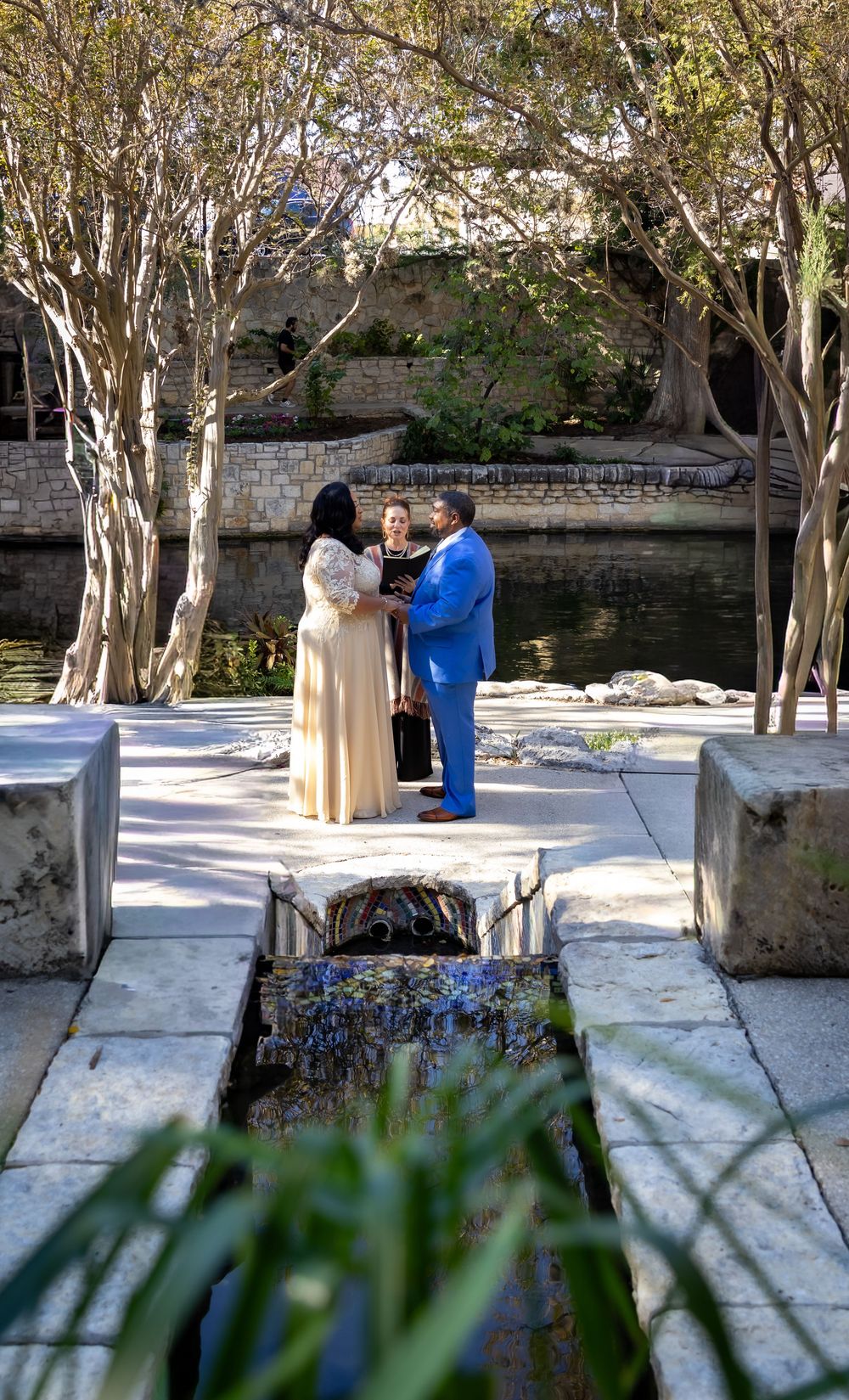 A couple stands together on stone paving near a water feature in a garden setting with birch trees.