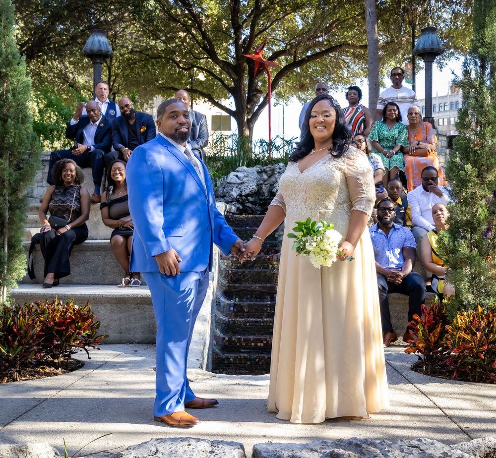 A couple in blue and cream attire poses for photos during their outdoor wedding ceremony at a tropical venue.