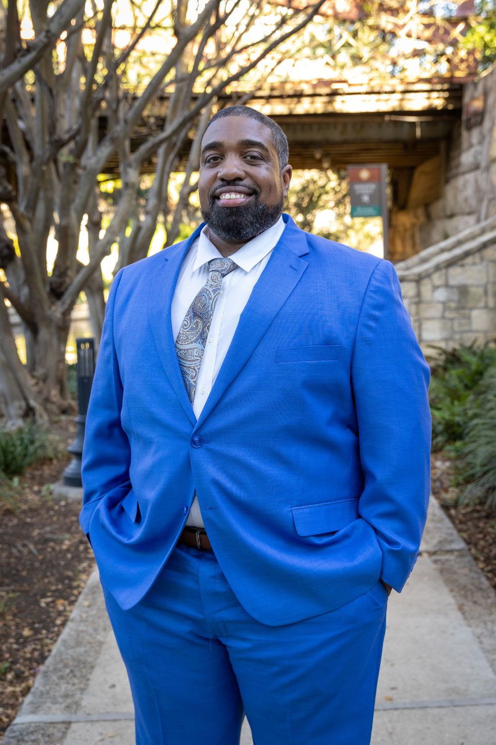 A person in a bright blue suit and patterned tie poses outdoors in a series of candid shots.