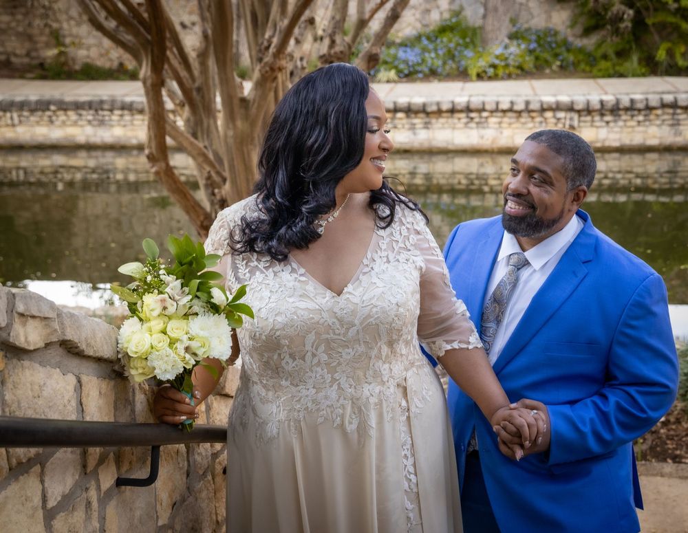 A couple in wedding attire shares a tender moment in a garden setting, with the bride in white and groom in blue.
