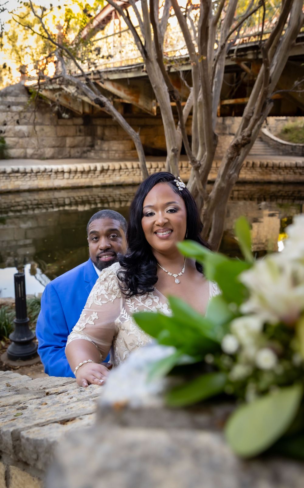 A couple shares joyful moments during their engagement photoshoot along a rustic stone wall surrounded by trees.