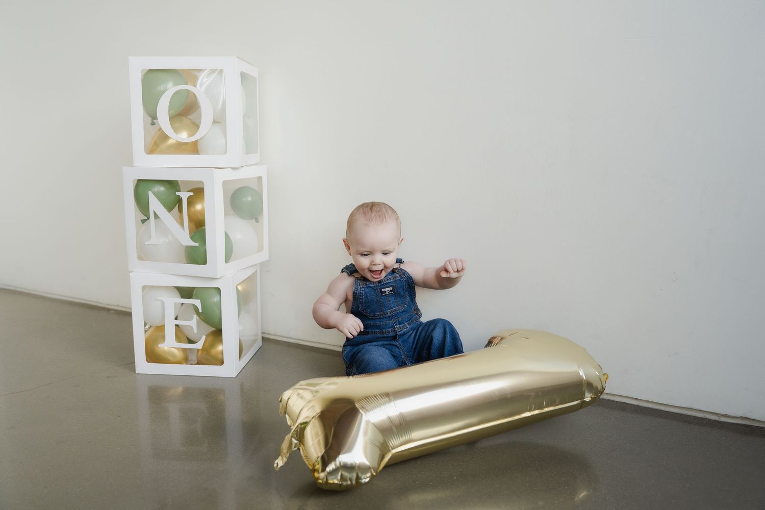 A small child in blue clothing crawls on a gold metallic blanket near white decorative cubes.