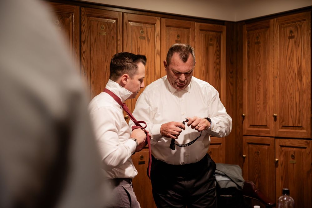 Two men in white shirts examine small objects in a wood-paneled room.